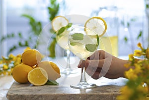 Citrus iced lemonade in pitcher and lemons glasses with lemon slice decoration and on marble table hand with cocktail