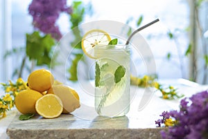 Citrus iced lemonade in pitcher and lemons glasses with lemon slice decoration and on marble table with lilac flowers