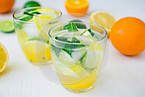 Citrus lemonade with lime, mint leaves and lemon in glasses on white table