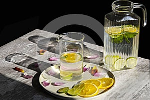 Citrus and mint lemonade in a jug and a jar standing on the table with some flower petals around in daylights