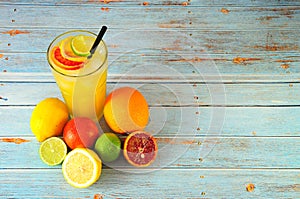 Citrus mix in a tall glass with ice, next to lime, lemon, orange and grapefruit on a wooden table