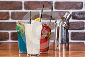 Citrus and raspberry lemonades, PiÃ±a colada and a shaker on a wooden table in a cafe.