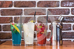 Citrus and raspberry lemonades, PiÃ±a colada and a shaker on a wooden table in a cafe.