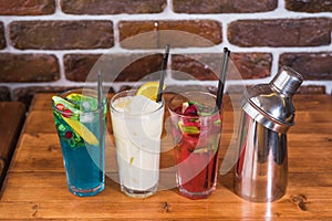 Citrus and raspberry lemonades, PiÃ±a colada and a shaker on a wooden table in a cafe.