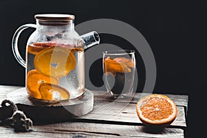 Citrus tea in a transparent teapot and a glass, healthy drink on a wooden background.