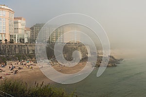 The city beach with golden sand and blue water is covered with fog, poor visibility.