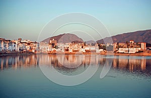 City with deep blue lake in India. Mountains around Pushkar at meditation calm mood with old houses around