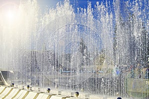City fountain with water jets and random people, view through splashes on Sunny summer day