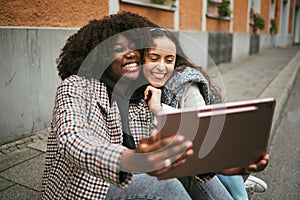 City, friends and women take selfie on tablet while sitting on sidewalk laughing and happy together. Photo, video call