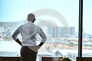 This city inspires me to keep upping my game. Rearview shot of a businessman looking out the window in an office.