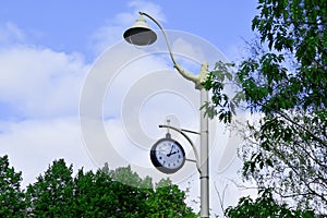 City lamppost with a modern lamp and round street clock showing 02:05 p.m., against blue sky