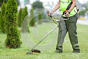 City landscaper worker cutting grass with string lawn trimmer
