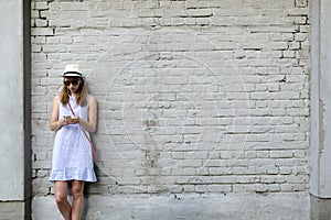 City life concept. Young woman standing next to the white brick wall listening to music in headphones