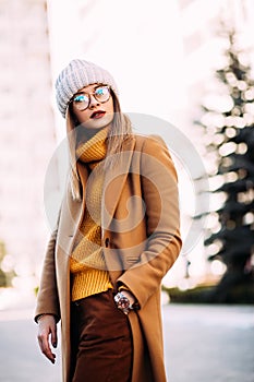 City lifestyle.Outdoor portrait of young beautiful woman Model wearing stylish glasses,mustard sweater, beige coat and grey