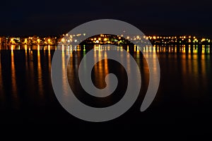 City lights are reflected on the water surface, a narrow line of light on the horizon