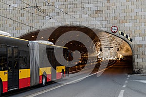 The city long bus drives into the tunnel under the bridge.