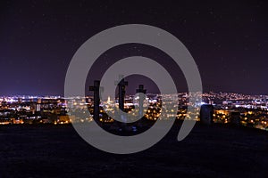 Mestská noc v Nitre z vyhliadky na vrchole kopca Slovenské mesto Nitra s fialovou nočnou oblohou a krížmi. Centrum mesta