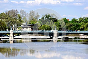 City park in Budapest. Small pond or lake with green steel bridge over. Lush green trees. Reflecting sky and white clouds. Leisure