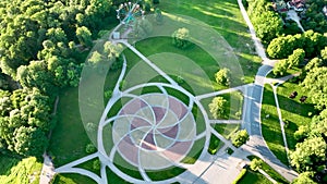 In a city park covered with trees and grass, with paths for walking, in the middle of the park there is a circle.