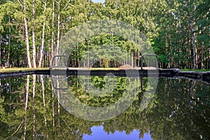 City park, metal trough filled with water. Reflection of trees and sky in the water