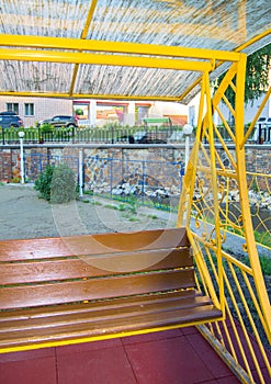 City Park in summer, empty wooden swing with yellow decorative metal frame, outdoor leisure furniture, vertical frame