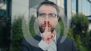 City portrait Caucasian business man businessman outdoors showing silence hush lips gesture keep secret secrecy