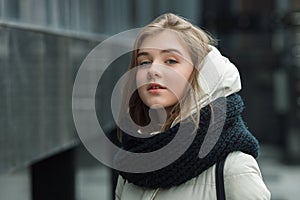 City portrait of young beautiful blonde stylish girl posing in spring fall outdoors in white coat black knitted scarf. Vintage fil