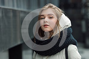 City portrait of young beautiful blonde stylish girl posing in spring fall outdoors in white coat black knitted scarf. Vintage fil