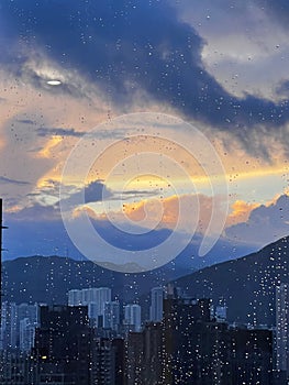 City skyline  against a sunset sky, illuminated by the rain droplets cascading down a window