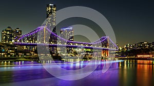 a city skyline with a bridge, lights and water in the foreground