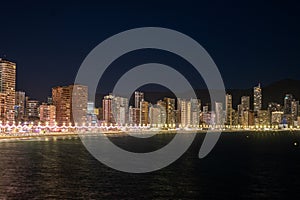 City skyline at night, with the promenades lights twinkling like stars against the dark sea, under a clear sky.