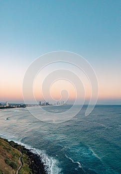 a city skyline overlooks the water from the coast with grassy hills to the ocean