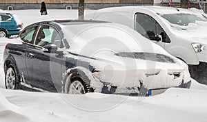 City street after blizzard. Stuck cars under the snow and ice. Buried vehicle in snowdrift on the road. Parking lots in