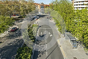 A city street with a median lined with trees, hedges and plant