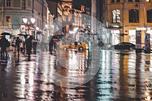 City street in rainy late evening, abstract background of blurred people figures under umbrellas. Intentional motion