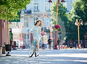 City street on summer day. Graceful girl rides bicycle