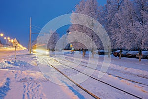 A city street on a winter early morning with snow-covered infrastructure and picturesque frost-covered trees. Twilight.