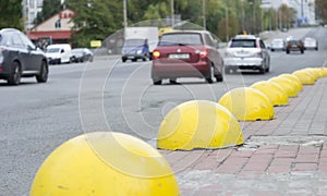 City traffic view from sidewalk with yellow spheres.