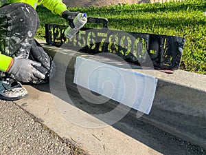 City worker painting address on street curbs using stencil numbers