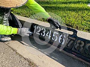 City worker painting address on street curbs using stencil numbers