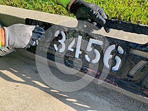 City worker painting address on street curbs using stencil numbers