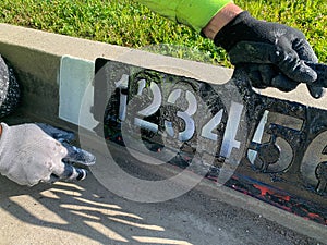 City worker painting address on street curbs using stencil numbers