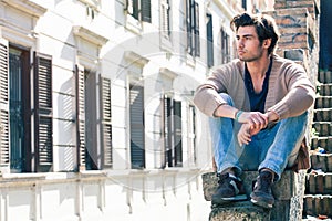 City young handsome man. Urban sitting model. Building windows