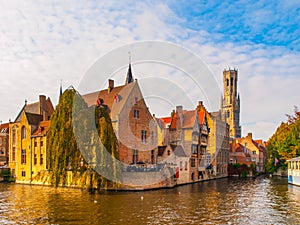 Cityscape of Bruges, Flanders, Belgium. Water canal at Rozenhoedkaai with old brick buildings and Belfry Tower on photo