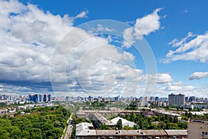 A cityscape with a green park in an old residential area of the city and new buildings on the horizon against a bright blue sky