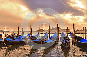 Cityscape with venice blue gondolas on st. mark`s square docks and cloudly sunset on St. Giorgio island with warm colors in backgr