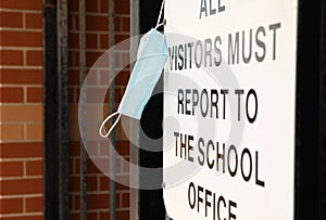 A civid-19 style protective mask hanging off a white sign outside at the entrance to a school ground. photo