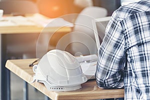 Civil construction engineer working with laptop at desk office with white yellow safety hard hat at office on construction site.