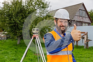 A civil engineer with an optical level approves the work of his colleagues with a smile by raising his hand