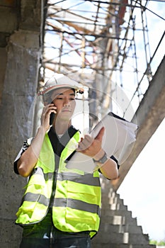 Civil engineer standing at construction site and having phone conversation